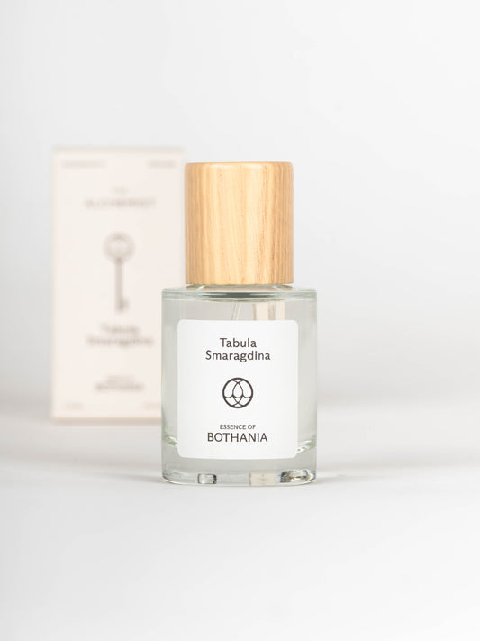 Clear glass bottle with wooden cap labeled 'Tabula Smaragdina' on a white background with the packaging behind it
