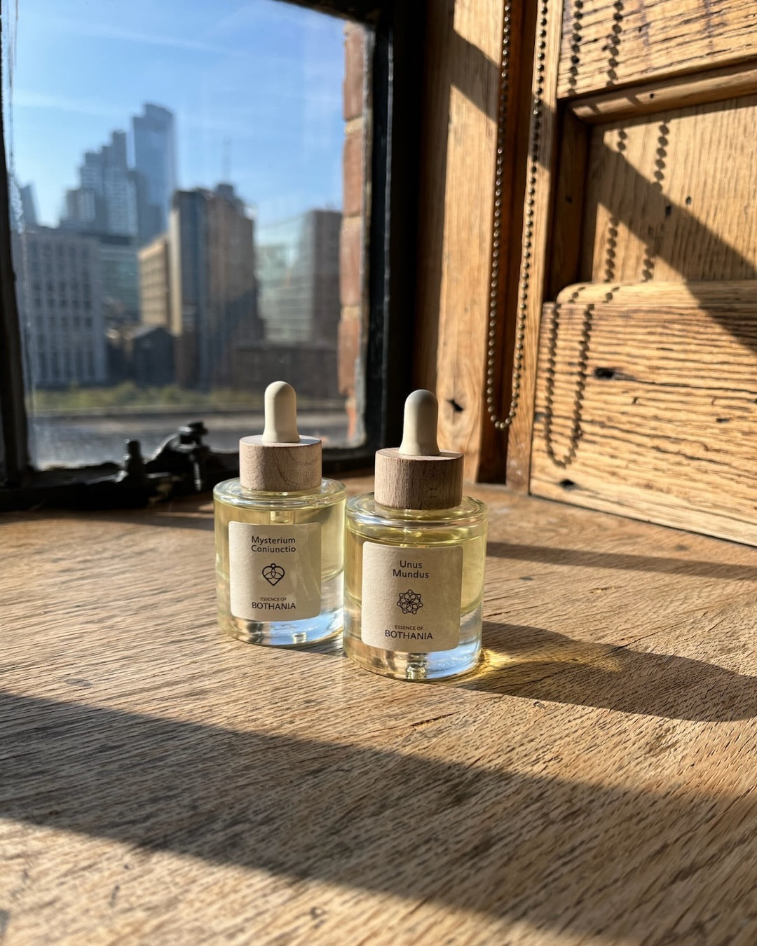 Two glass bottles with wooden dropper lids on a wooden surface with a cityscape in the background.