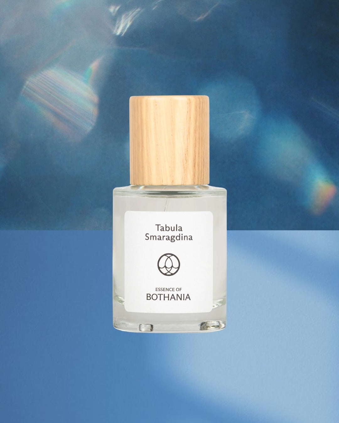 Bottle of 'Tabula Smaragdina' made by House of Bothania. A glass bottle with wooden cap on a blue background. Bio-energetic perfume made to awaken our senses. Tabula Smaragdina connects us to the throat chakra. Awakens intuition. Evokes clear and peaceful communication. Speak your truth with integrity.