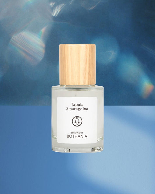 Bottle of 'Tabula Smaragdina' made by House of Bothania. A glass bottle with wooden cap on a blue background. Bio-energetic perfume made to awaken our senses. Tabula Smaragdina connects us to the throat chakra. Awakens intuition. Evokes clear and peaceful communication. Speak your truth with integrity.