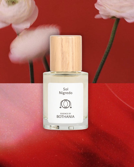 Bottle of Sol Nigredo made by House of Bothania, on a red background with flowers. Bioenergetic perfume made to awaken your senses. Connected to the root chakra. Enhances grounding, stability and connecting to your roots.