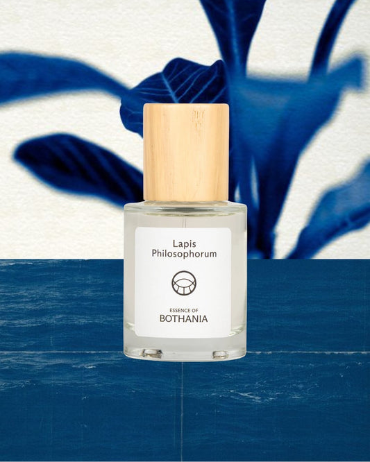 Bottle of 'Lapis Philosophorum' by Bothania. Glass bottle with a wooden cap on a blue and white background. Bioenergetic perfume made to awaken your senses. Lapis Philosphorum is connected to our Third Eye, and enhances the ability to see beyond. A deeper understanding and connection with the universe.
